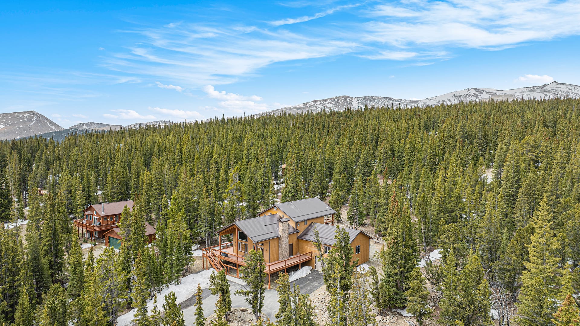 Aerial view of the home among pines with snowy peaks beyond