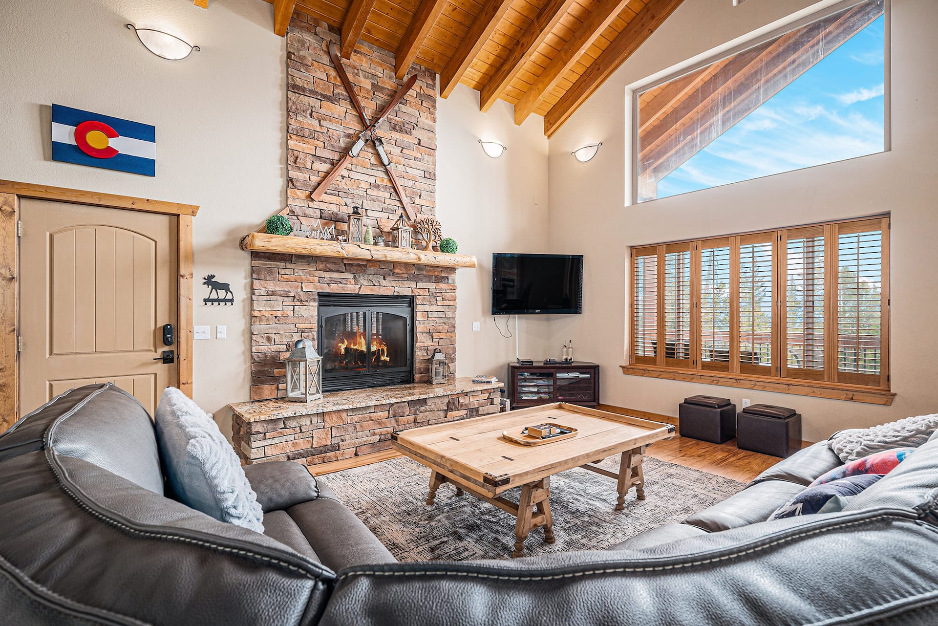 Stone fireplace with crossed skis beside a leather sectional and tall windows