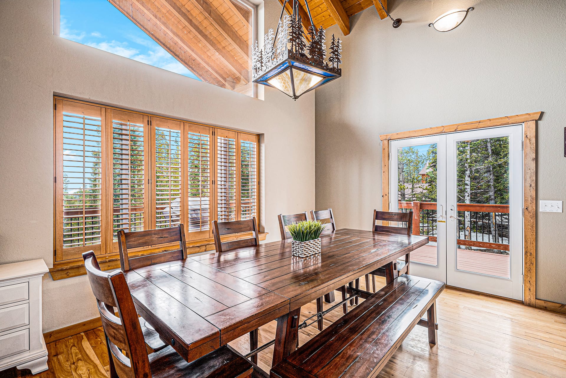 Long wooden dining table with a bench and French doors to the deck